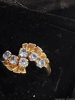Close-up of the ladies gold ring showing the six light blue stones with gold prong settings and band marked 10K.