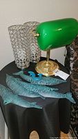 Shows two crystal-embellished bedside lamps, green banker's lamp, and four metal sea-themed wall art pieces on cloth-covered table