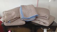 Brown quilted bed coverlets with smooth backs folded on furniture