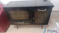Front view of the dark wood Mid-Century Modern hope chest showing left lid and right cupboard door closed, with metal handles and tapered legs.