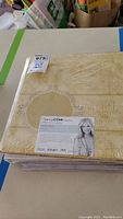 Close view of beige Nancy O'Dell Collection 12x12 scrapbook album with embossed decorative pattern and label showing collection and size.