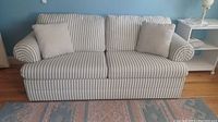 Front view of the blue and white striped sleeper sofa with two matching cushions placed on it.