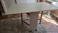 Full view of the white double drop leaf cutting table with castor wheels, surface in expanded position.
