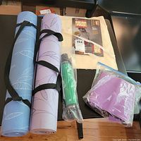 Full lot overview showing two rolled yoga mats, electric heating pad packaging, Curves waist trimmer in plastic, and Thera-Band band.