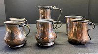 Front angled view of six antique handmade Turkish copper cups showing hammered texture and varied handles made of brass and copper.