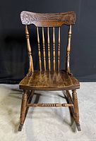 Front view of antique pressed back oak rocking chair showing carved top rail and spindle backrest.