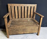 Front view of antique oak storage bench showing vertical slat backrest and flat armrests.