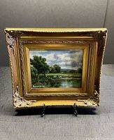 Frontal view of the oil painting depicting cows by the lake, showing the signature and detailed frame.