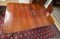 Top view of closed Bernhardt mahogany dining table on red patterned rug, showing wood grain and surface wear.