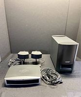 Front view of Bose system showing Media Centre control unit, two small bookcase speakers on stands, and large Acoustimass subwoofer with Bose logo.