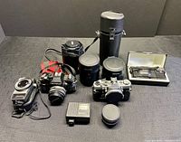 Lot overview with cameras, lenses, cases, flash, teleconverter and filters arranged on table