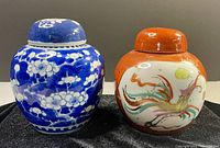 Photo of two Chinese ginger jars, one blue and white with Hawthorne design and one orange with dragon design, both with lids and placed on a black cloth.