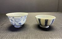 Front view of two porcelain tea cups side by side on gray fabric, showing shape and patterns
