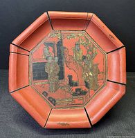 Top view showing the octagonal shape and central painted vignette of women in traditional garb on a red lacquer background, with sections tied by cord and visible wear.