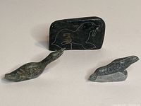 Photo showing all three soapstone carvings together: the slab with seal etching, loon carving, and seal carving