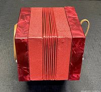 Closed red pearloid concertina resting on black surface showing compressed bellows and hexagonal end panels.