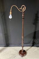 Full view of the floor lamp showing wooden turned base and wrought iron arm with decorative scrollwork, hanging bulb socket, pull switch chain, and cord.