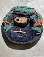 Full view of Outfitters fly fishing float tube in green, black and orange, with woven cane creel and fish cutting tool with leather scabbard placed inside