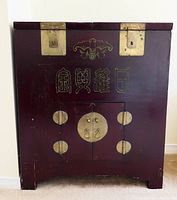Front view of large antique Chinese wood money chest with bat motif and Chinese characters carved or inlaid in brass on front. Shows brass lock plates and hinges.