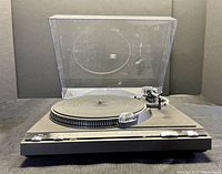 Front-angle view of turntable with dust cover open showing platter, tonearm, controls