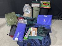 Wide shot showing assorted camping equipment including rolled mats, mesh netting, repair kit, bags, and cords.
