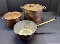 Three vintage Turkish hand-hammered copper cooking pots shown together: one saucepan with long brass handle, two stock pots with lids and brass handles, photographed from front and side angles.