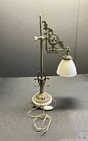 Full view of lamp showing brass stand, decorative arm with bird medallion, alabaster base, milk glass shade, and cord with switch.