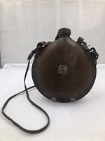 Front view of the round leather canteen with attached shoulder strap and screw-top lid.