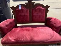 Full front view of red velvet upholstered loveseat with carved wooden frame
