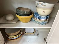 Shelved collection showing stacked bowls, plates, and bakeware including a yellow bowl, green bowl, and bowls with floral detailing