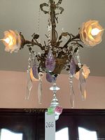 Front view of three-arm chandelier showing frosted glass flower shades, hanging crystal prisms and purple glass accents.