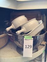 Photo showing large cream-colored mixing bowl with vegetable motif and several white handled mixing bowls placed inside a metal colander.