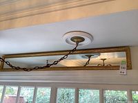 Full view of the long rectangular mirror showing the gold ornate frame and its placement above a window with a chain hanging from ceiling fixture reflected within.