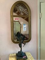 Full view of the oval mirror mounted on wall with bronze Cupid statue on marble base in front