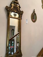 Full view of large gilded ornate mirror with carved urn and floral crest, showing mirror surface and surrounding frame