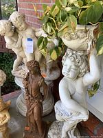 Angled close view showing the cherub statue holding a planter above and the lady figurine in front, highlighting material and texture.