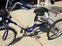 Left side profile view of blue three-wheel bicycle showing frame, front wheel, saddle and pedals