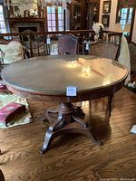 Front view of round wooden dining table with glass top and central pedestal base