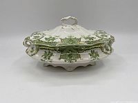 Side angle photo of the covered tureen showing green floral patterns, gold trim, and the ornate lid handle.