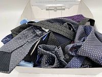 Box filled with assorted men's neckties showing a variety of dark colors and patterns including geometric and floral prints, from top view.