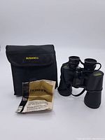 Photo showing binoculars, black carrying case with Bushnell logo, and unfolded instruction sheet.