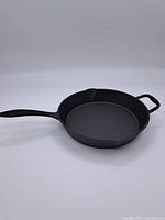 Side angle showing the entire cast iron frying pan with handle and pouring spout