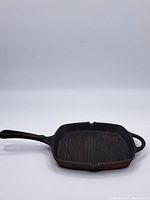 Full view of vintage square cast iron pan showing long handle, helper handle and ridged cooking surface.