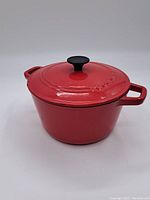 Red enameled cast iron Dutch oven with lid and black knob, showing embossed 'Cuisinart' branding on the lid.