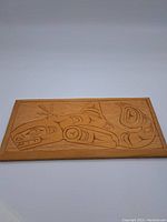 Front view of rectangular hand carved yellow cedar wood plaque with stylized animal figure in Kwakiutl design.