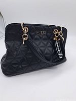 Front angle view of the GUESS handbag showing its quilted pattern and attached handles with gold hardware.