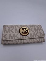 Full front view of beige wallet showing all-over MK print and gold-tone MK emblem on the flap