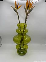 Full view of large green glass bauble-shaped vase with three artificial Bird of Paradise flowers inside.