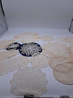Photo showing a collection of multiple antique crocheted and tatted lace doilies of varying sizes and patterns laid flat on a white surface.