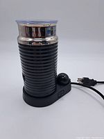 Front view of the Nespresso black and silver Aeroccino frother on its black base with power cord and switch visible.